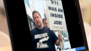 Bildschirmansicht eines Mannes, der ein Schild hält auf dem eine Verschwörungstheorie über den 11. September steht.