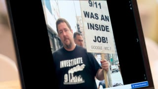 Bildschirmansicht eines Mannes, der ein Schild hält auf dem eine Verschwörungstheorie über den 11. September steht. Bildschirmansicht eines Mannes, der ein Schild hält auf dem eine Verschwörungstheorie über den 11. September steht.