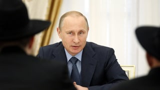 Putin sitzt zwei Männern mit Hut gegenüber und spricht mit ihnen. Putin sitzt zwei Männern mit Hut gegenüber und spricht mit ihnen.