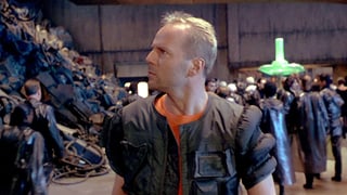 Bruce Willis geht durch eine Halle an einem Müllberg vorbei.