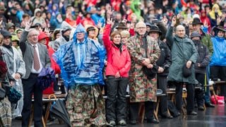 Bürger mit Regenschutz strecken den Arm hoch an der Landsgemeinde in Glarus.
