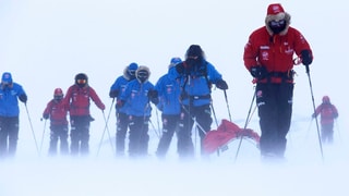 Prinz Harry und acht weitere Expeditionsteilnehmer in Anzüge eingehüllt auf Skiern im Schnee.