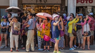 Eine grosse Gruppe von Touristen mit Sonnenschirmen und Handykameras.