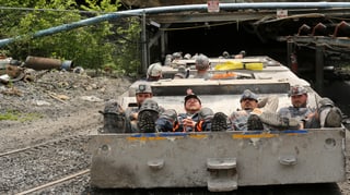 Minenarbeiter liegen auf einem niedrigen Wagen, der in den Bergstollen fährt.