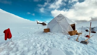 Zelt auf einer Eisfläche. Im Hintergrund ein Helikopter.