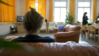 Eine Frau von hinten sitzt auf einem Sofa.