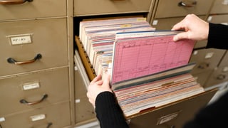 Zwei Hände ziehen eine Akte aus einem geöffneten Archivschrank des Stadtarchivs Bern heraus.
