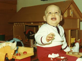 Baby-Junge sitzt erfreut vor Spielzeug-Stall.