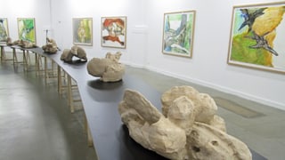 Sieben Holzskulpturen in der Mitte des Raumes, an der Wand hängen Pastell-Bilder. Sieben Holzskulpturen in der Mitte des Raumes, an der Wand hängen Pastell-Bilder.