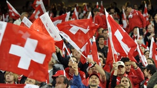 Fussball-Fans in rot-weiss gekleidet schwingen Schweizerfahnen.