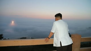 Kim in weissem Hemd, durch die Wolken bricht eine startende Rakete.