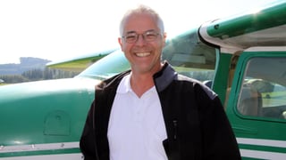 Pascal Miller mit Brille, weissem Hemd und dunkler Weste steht vor einem grünen Sportflugzeug.