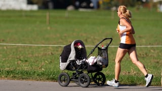 Frau joggt mit Kinderwagen bei Sonnenschein.
