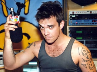 Robbie Williams im Muskelshirt mit Mikrofon.