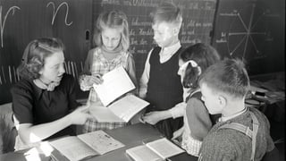 eine schwarz-weiss Fotografie einer Lehrerin, die ihren Schülern etwas am Pult zeigt eine schwarz-weiss Fotografie einer Lehrerin, die ihren Schülern etwas am Pult zeigt