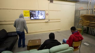 Drei Männer sitzen auf dem Sofa und schauen TV.