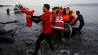 Ein Mitarbeiter des Roten Kreuzes trägt ein Baby von einem Flüchtlingsboot. Ein Mitarbeiter des Roten Kreuzes trägt ein Baby von einem Flüchtlingsboot.