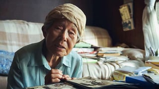 Eine alte Frau sitzt an einem Tisch vor einem Fotoalbum.