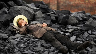 Mann ruht sich auf Kohlehaufen aus. 