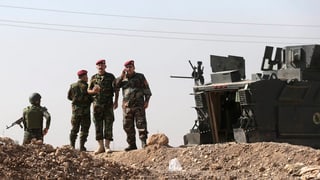 Irakische Offiziere stehen bei einem gepanzerten Fahrzeug.
