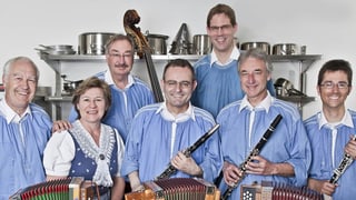 Die Musikanten tragen blaue Kutten und stehen mit ihren Instrumenten in einer Küche.