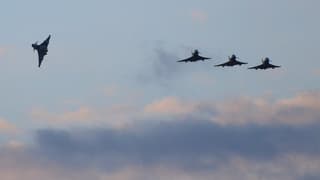 Vier Kampfflugzeuge am Himmel, im Hintergrund Wolken.
