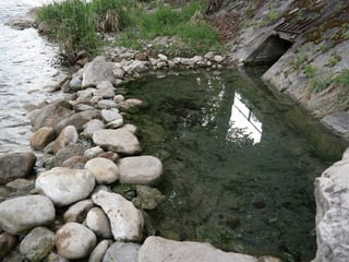 Wasser fliesst in einen Fluss zwischen Steinen.
