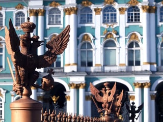 Eine Nahaufnahme des Winterpalasts: eine Adlerskulptur auf einem Zaun, im Hintergrund das türkis-weiss-goldene Gebäude.
