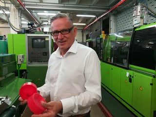 Mann hält rote Plastik-Teile in der Hand. Grüne Maschinen im Hintergrund.