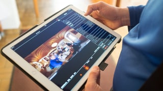 Ein Mann hält in seinen Händen ein Tablet, auf dem fotografische Informationen sichtbar sind. 