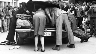 Ein Theaterstück: Leute schauen unter die Motorhaube eines Autos. Im Hintergrund: Publikum. Ein Theaterstück: Leute schauen unter die Motorhaube eines Autos. Im Hintergrund: Publikum.