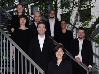 Die in Schwarz-Weiss gekleideten Sängerinnen und Sänger posieren fürs Gruppenbild auf einer Treppe.