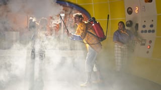 Ein Mann hält eine Art Feuerlöscher, aus dem es dampft, im Hintergrund drückt jemand auf einen Knopf. Ein Mann hält eine Art Feuerlöscher, aus dem es dampft, im Hintergrund drückt jemand auf einen Knopf.