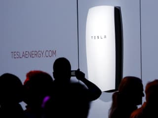 Silhouetten von Menschen vor einer Grossbatterie, die von der Firma Tesla entwickelt wurde. Silhouetten von Menschen vor einer Grossbatterie, die von der Firma Tesla entwickelt wurde.
