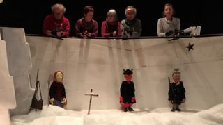Bühne mit grossen Marionettenfiguren und im Hintergrund die Spieler, die die Puppen halten. 