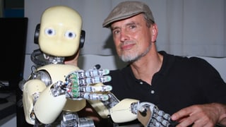 Schmidhuber posiert mit einem Roboter mit niedlichen, kindlichen Gesichtszügen.