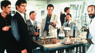 Eine Gruppe von Männer hält in einem Chemielabor einen Mann mit Waffengewalt fest.