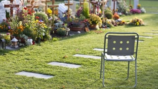 Ein leerer Stuhl steht vor frischen Gräbern.