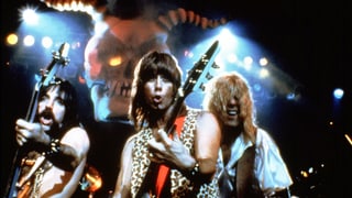 Drei Männer mit langen Haaren und Gitarren auf einer Bühne