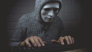 Maskierte Person an einer Tastatur.
