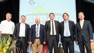 SVP-Männer rund um Präsident Toni Brunner singen auf der Bühne die Nationalhymne. 