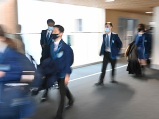 Schüler laufen in Uniform und mit Maske einen Gang entlang. 