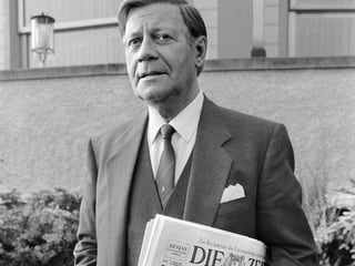 Schwarz-Weiss-Aufnahme von Helmut Schmidt mit einer Zeitung unter dem Arm. 