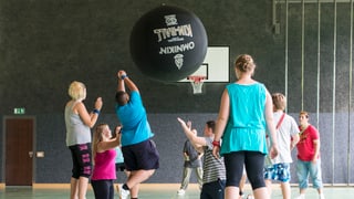Übergewichtige Jugendliche treiben in der Turnhalle Sport. 