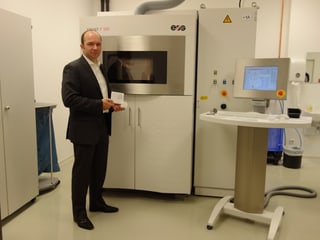 Ein Mann steht vor einem 3D Drucker, ein mannshohes Gerät.