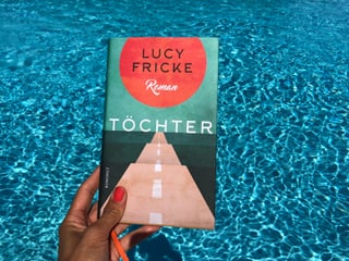 Annette König hält das Buch von Lucy Fricke: «Töchter» vor blaues Wasser Annette König hält das Buch von Lucy Fricke: «Töchter» vor blaues Wasser
