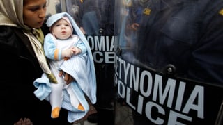 Eine Frau steht mit ihrem Baby vor den Schutzschildern der Polizei