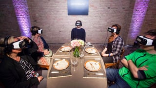 Menschen sitzen an einer gedeckten Tafel. Sie haben alle auf VR-Brille auf.