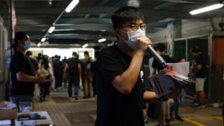 Wong trägt eine Hygienemaske, hat Flyer in der Hand und spricht in ein Mikrofon.