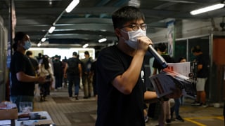 Wong trägt eine Hygienemaske, hat Flyer in der Hand und spricht in ein Mikrofon. Wong trägt eine Hygienemaske, hat Flyer in der Hand und spricht in ein Mikrofon.